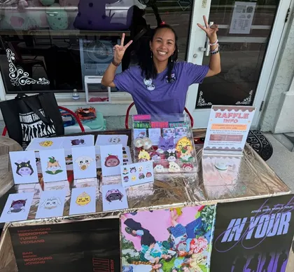 Host behind a themed-night merch table with photocards and raffle info